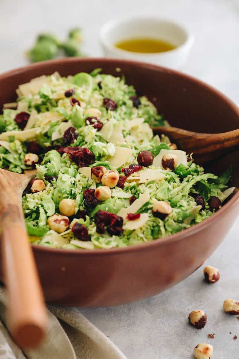 close-up image of shredded brussel sprout salad in a brown bowl with dried cranberries, parmesan cheese and toasted hazelnuts.