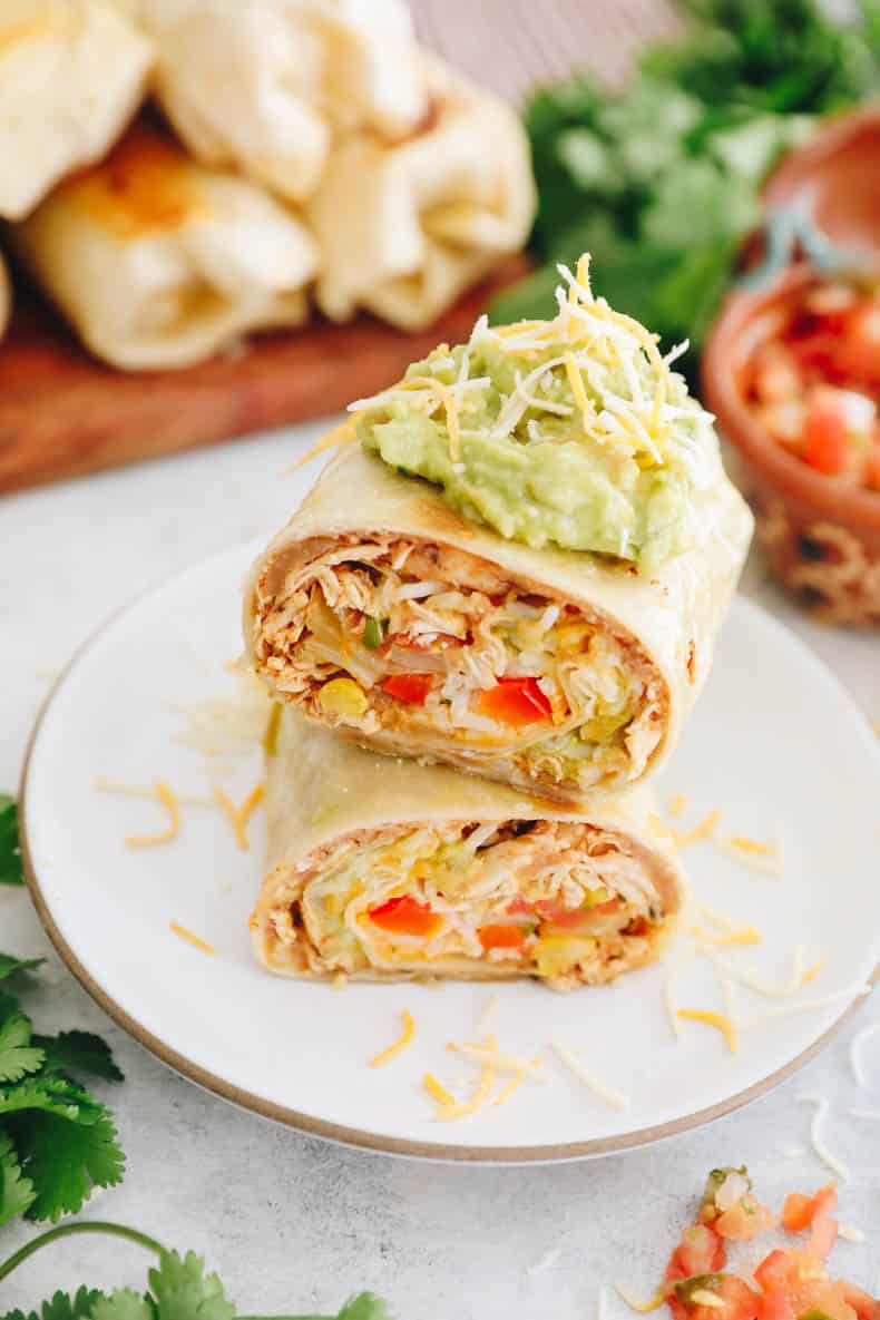 overhead of chicken burrito recipe topped with guacamole and shredded cheese.