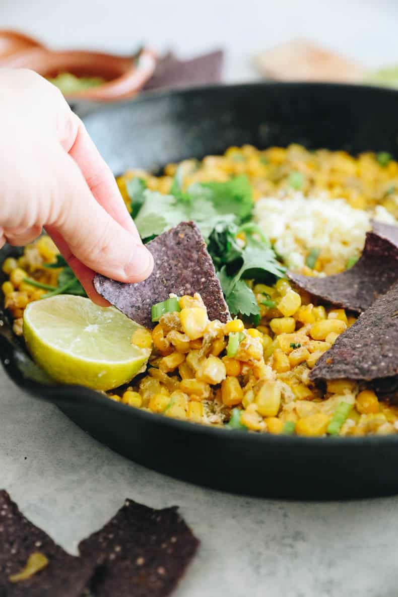 hand dipping a blue corn chip into Mexican Street Corn Dip