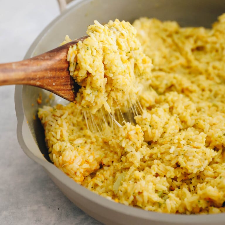 cheesy rice with hidden veggies in a pot with a wooden spoon.