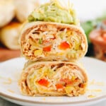 chicken burrito recipe cut in half and stacked on top of each other topped with guacamole and shredded cheese.