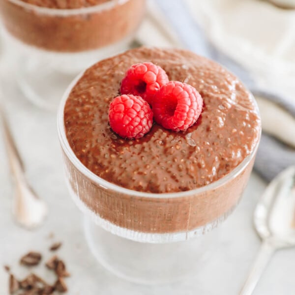 creamy chocolate chia pudding in a glass cup with fresh raspberries on top.