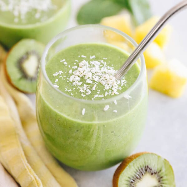 kiwi smoothie on a white table with a metal straw and sprinkled with coconut flakes.