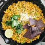 Mexican Street Corn Dip in a cast iron skillet with cilantro, cotija cheese, blue corn chips + lime