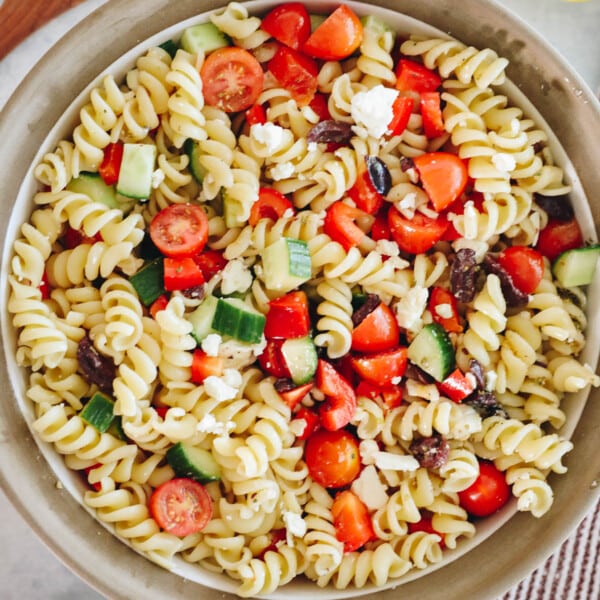 A large white and brown bowl with Greek pasta salad mixed together.