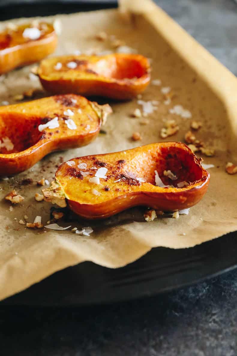 roasted honeynut squash on a sheet pan with coconut oil, cinnamon and salt and sprinkled with coconut flakes and walnuts.