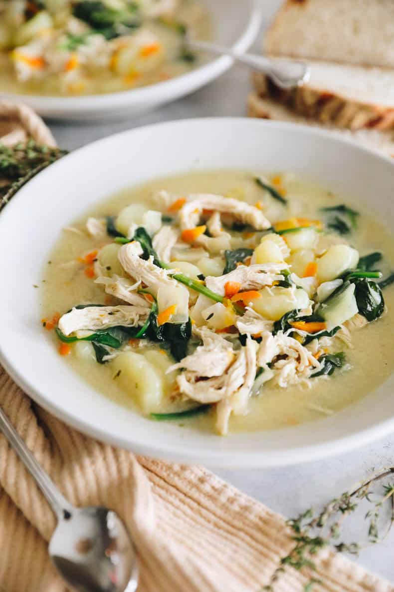 shredded chicken, potato gnocchi and spinach in a soup in a white shallow bowl.