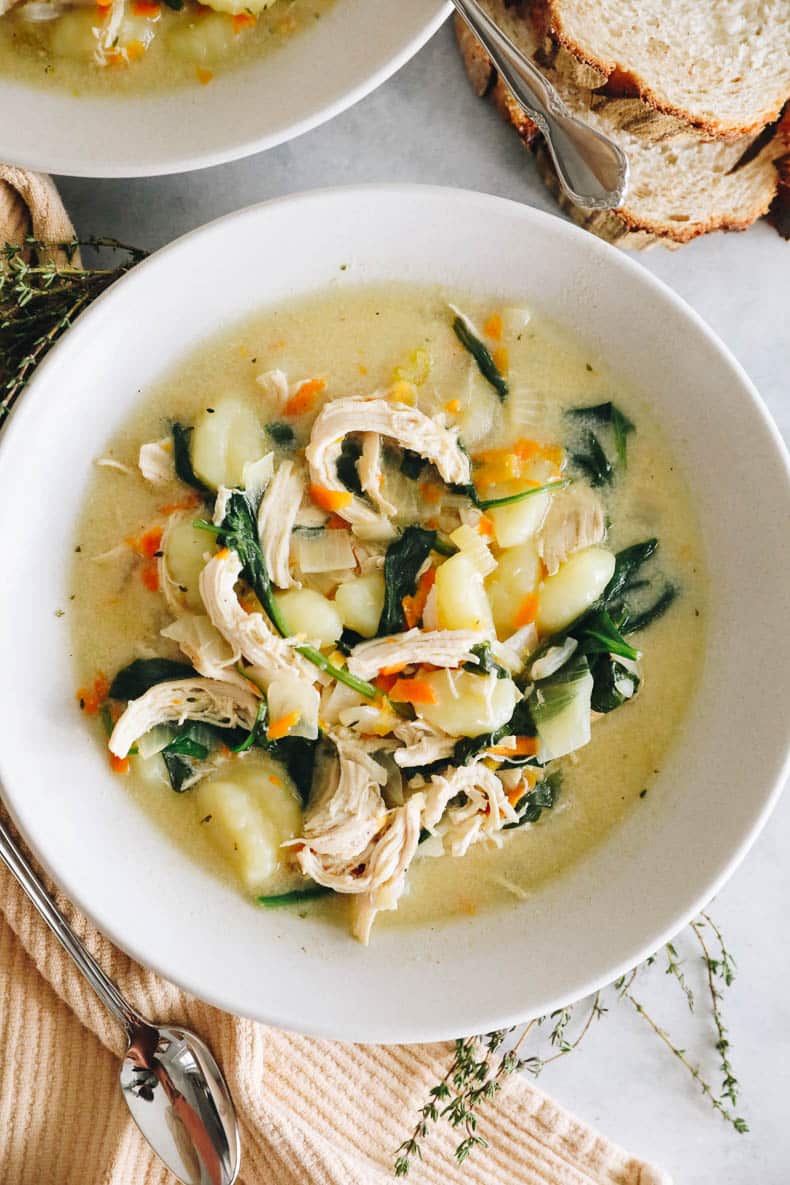 overhead image of chicken gnocchi soup in white bowls with bread on the side.