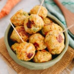 Baked chicken meatballs in a green bowl with toothpicks.