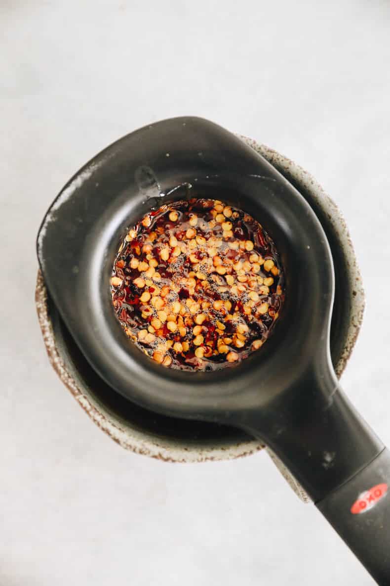 red chili flakes in honey being strained through a mesh sieve.