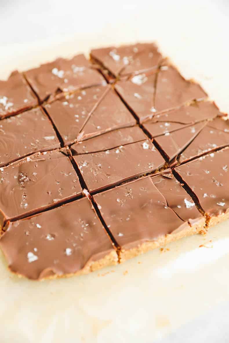 No bake chocolate almond butter bars cut into 12 squares on a sheet of parchment paper.