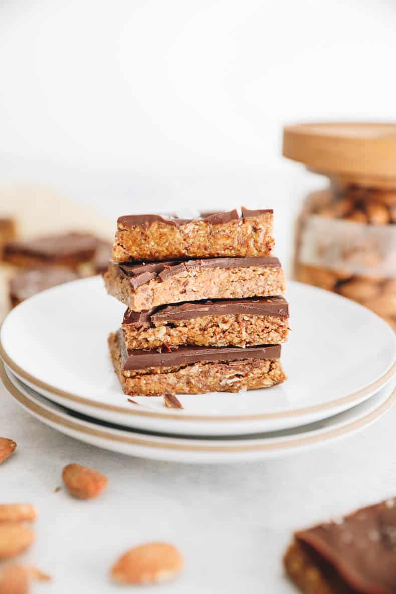 4 chocolate almond butter bars stacked on a white plate.