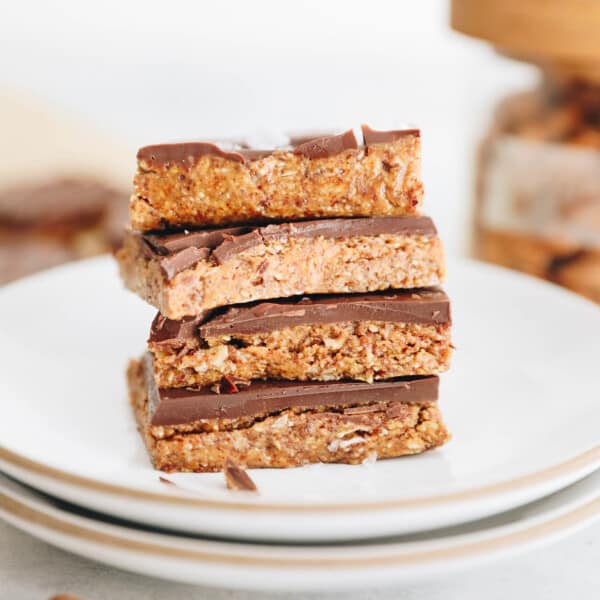 4 no bake chocolate almond butter bars stacked on top of one another on a white plate and sprinkled with maldon sea salt.