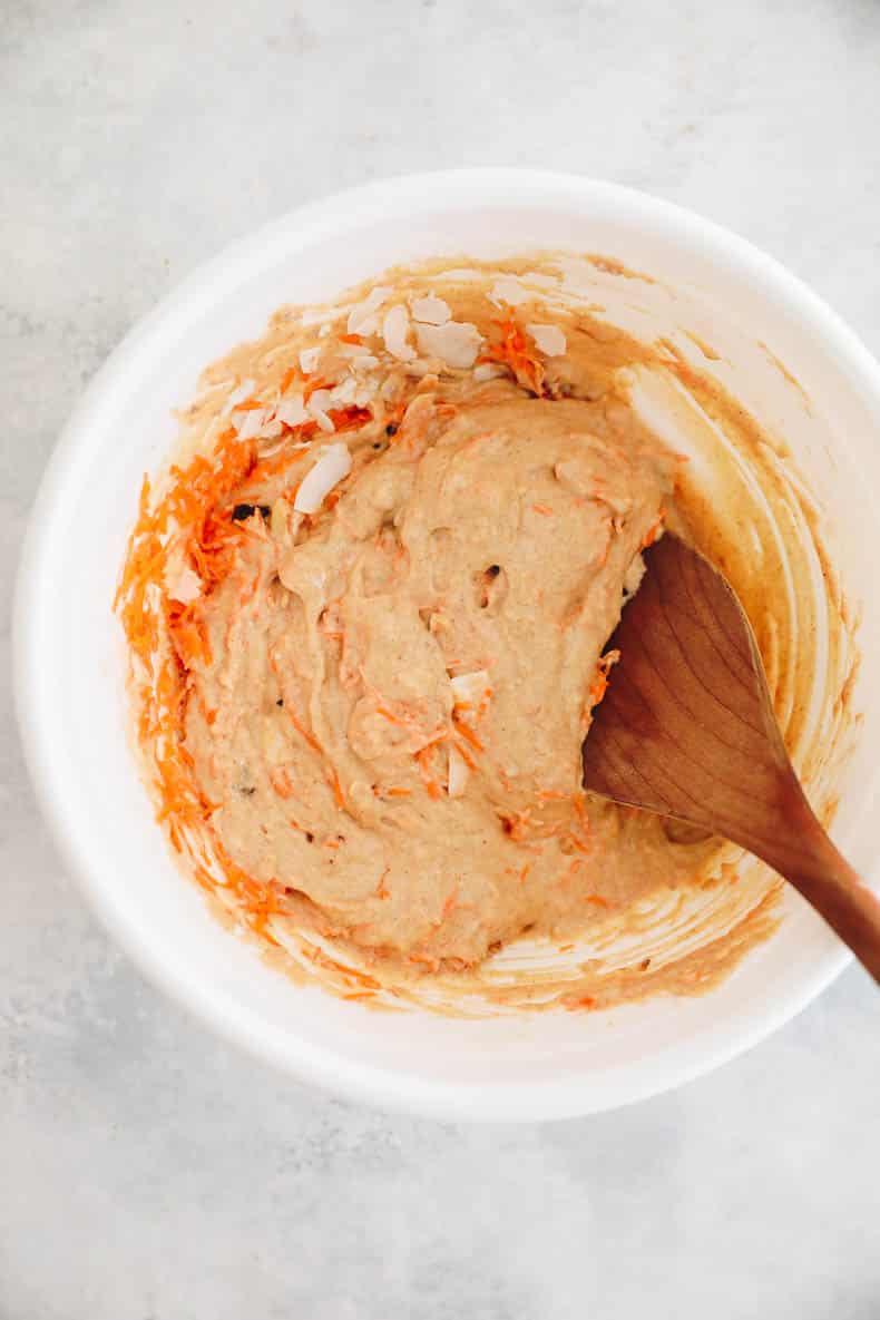 carrot cake pancake batter in a white bowl with a brown mixing spoon.