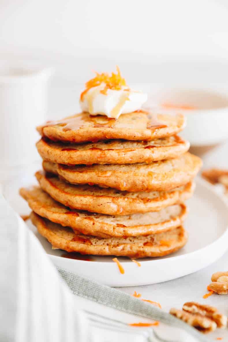 6 carrot cake pancakes stacked on top of each other in a white plate with yogurt and grated carrot.