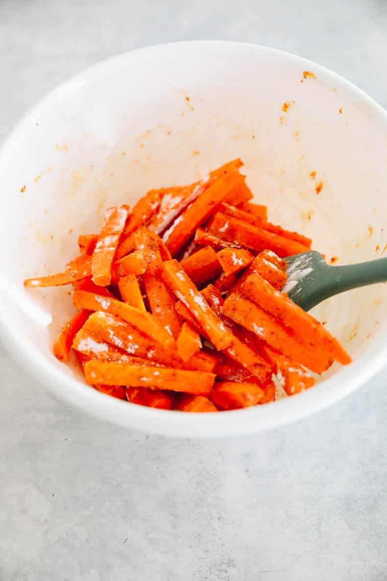 Carrot fries in a bowl with cornstarch and spices.