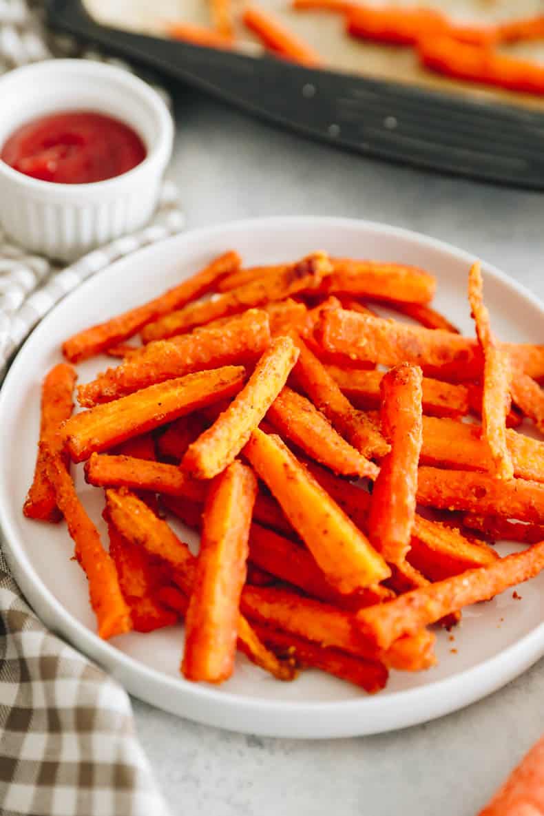 crispy baked carrot fries on a white plate with ketchup.