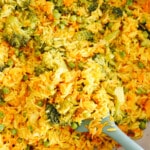 yellow curry rice with broccoli, peas and carrots in a caraway pot with a green spatula.