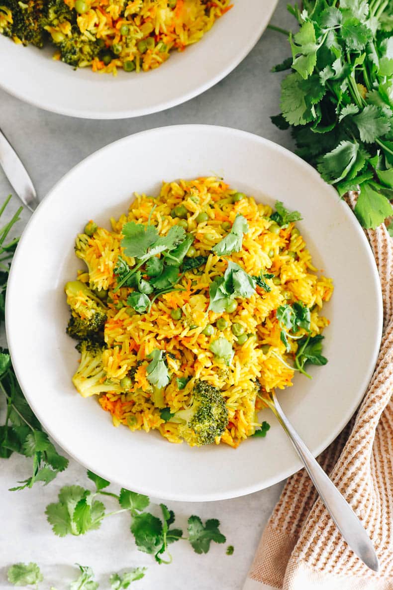 curried rice pilaf with veggies and cilantro in a white bowl.