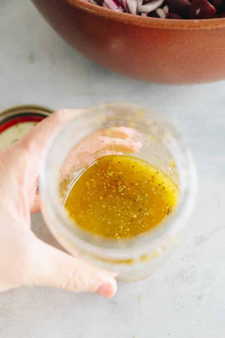 A hand holding Greek vinaigrette in a mason jar.