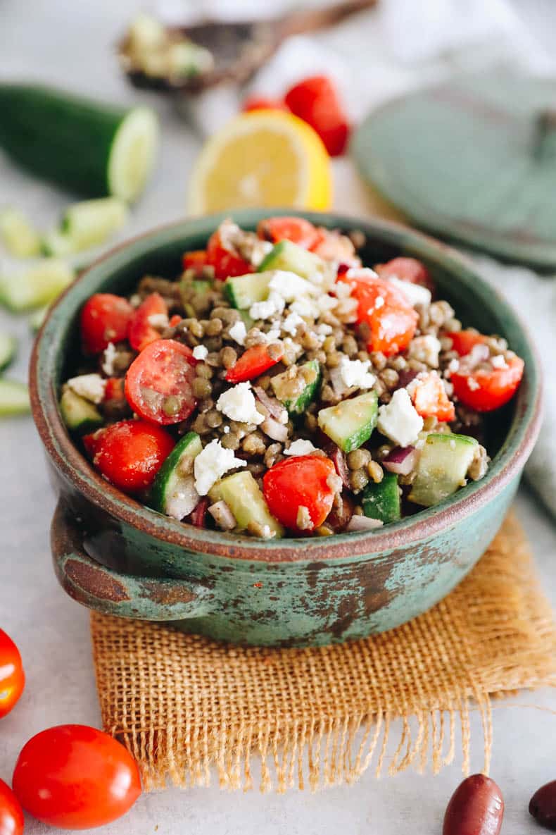 Greek lentil salad with tomatoes, peppers, cucumbers, onions and feta in a green bowl.