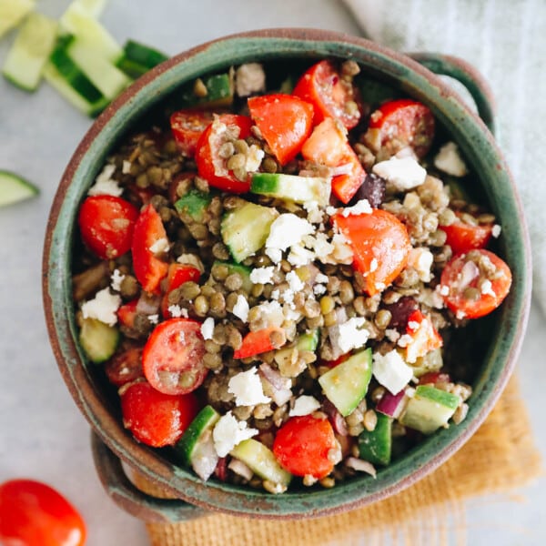 Hearty lentil salad with tomatoes, peppers, cucumber and feta in a large green serving bowl.