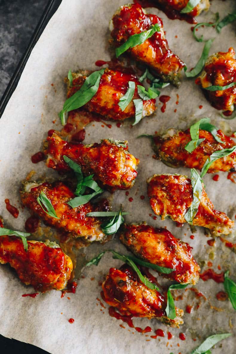 Baked thai basil wings on a sheet pan lined with parchment paper and topped with thai basil.