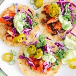 Overhead image of salmon tacos with avocado crema, jalapenos, cilantro, lime and cabbage.