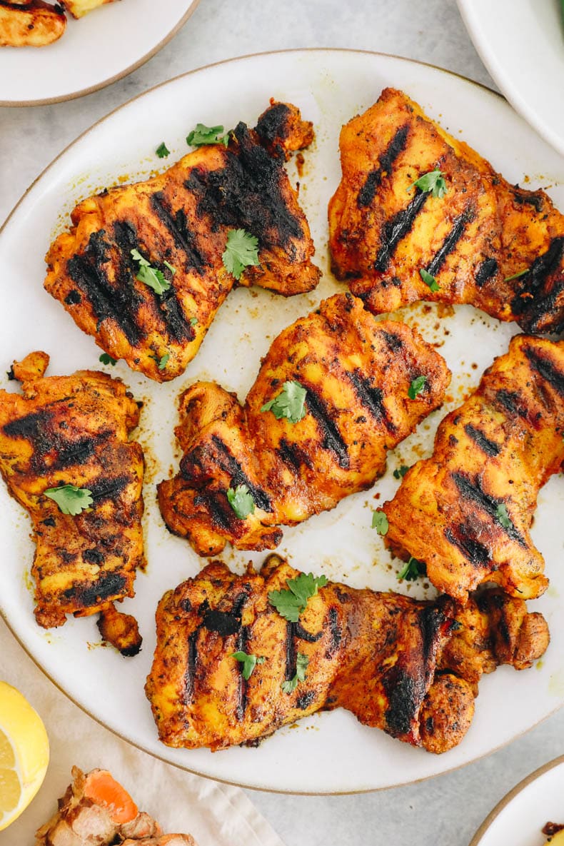 overhead of turmeric chicken thighs on a white plate.