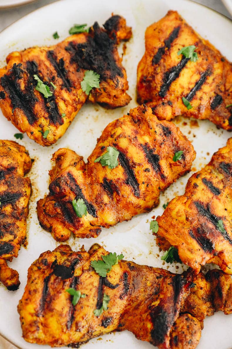 Close-up of grilled turmeric chicken on a white plate.