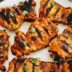 close-up of grilled turmeric chicken on a white plate and sprinkled with cilantro.